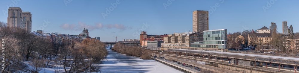 Panorama, water front buildings, iicy canal Karlbergskanalen, traffic route Karlbergsleden, train tracks, dome and tower buildings, bridge St Eriksbron a sunny day in Stockholm