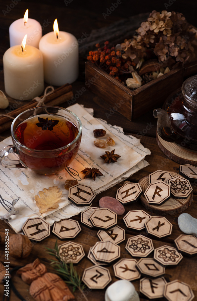 Wooden runes are lying on the table among the papers with notes. There is a mug of tea next to it. Astrology and esotericism.