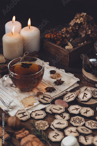 Wooden runes are lying on the table among the papers with notes. There is a mug of tea next to it. Astrology and esotericism.