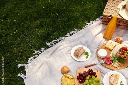 Fototapeta Naklejka Na Ścianę i Meble -  leisure, food and drinks concept - close up of snacks and picnic basket on blanket on grass at summer park