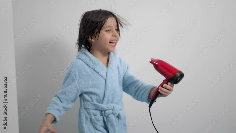 portrait of a five year old boy with long hair after a bath in a blue bathrobe and dries his hair with a red hairdryer , sings fooling around in the crib in the children's room before going to bed portrait of a five year old boy with long hair after a bath in a blue bathrobe and dries his hair with a red hairdryer , sings fooling around in the crib in the children's room before going to bed
