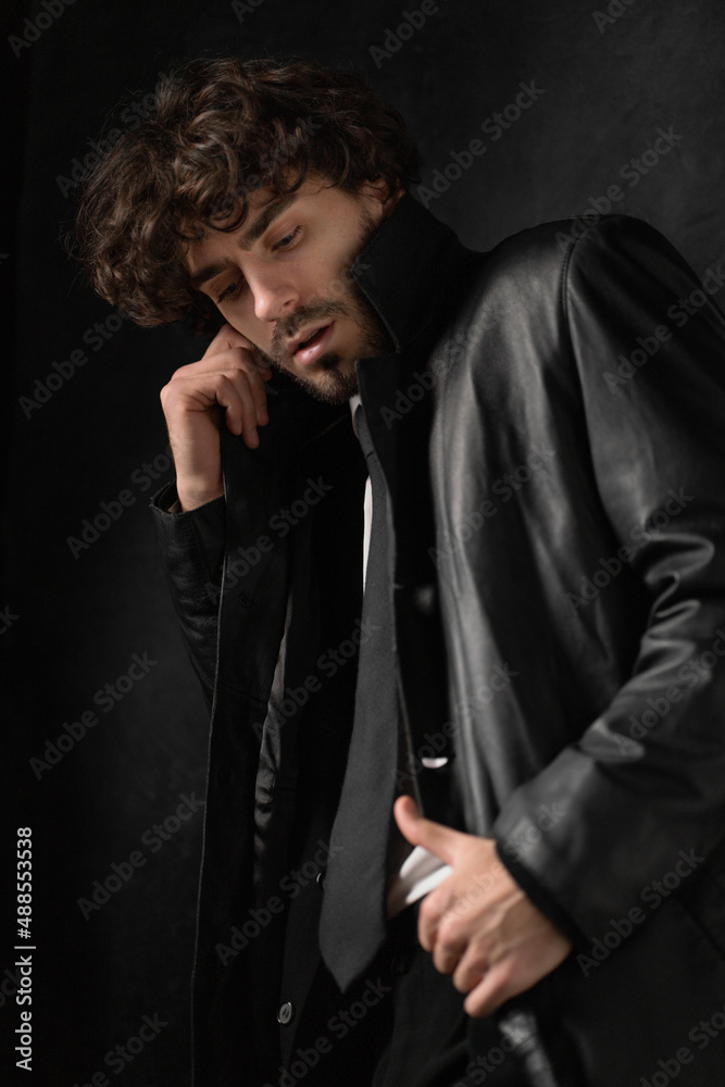 Young man with beard in white shirt and black leather coat against black background. High quality photo