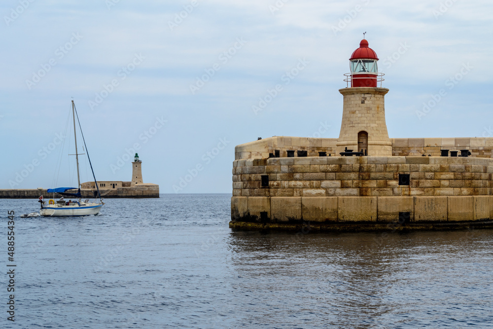 A sailing boat passing between the Ricasoli Breakwater lighthouse & Valletta Breakwater lighthouse at the entrance to the Grand Harbour in Malta