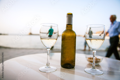 A bottle of white wine with two glasses in a harbour cafe in a summer night in Crete.