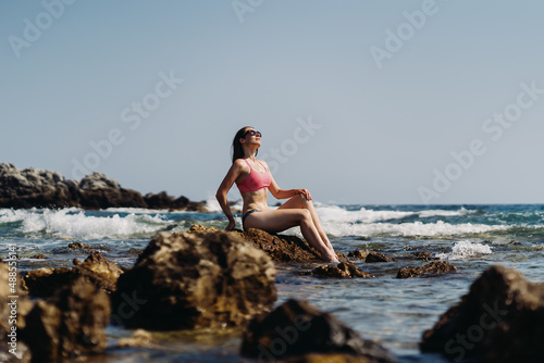 Happy young woman enjoying freedom on vacation while sitting on the coast rocks enjoying sea and blue sky view