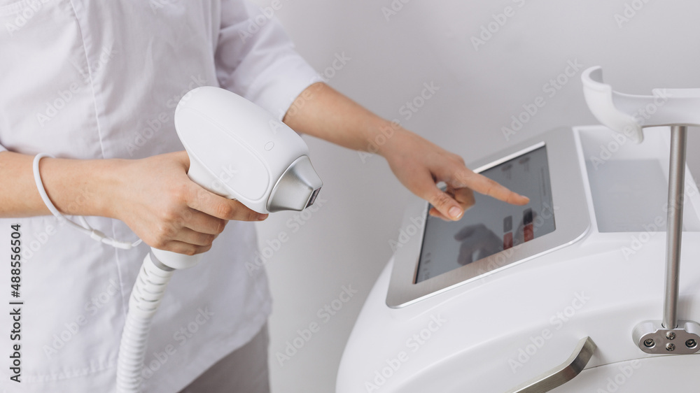 A woman tunes a laser hair removal machine. Girl holding a working part of  the epilator in her hands in a modern beauty salon. Underarm Laser Hair  Removal concept Stock Photo |