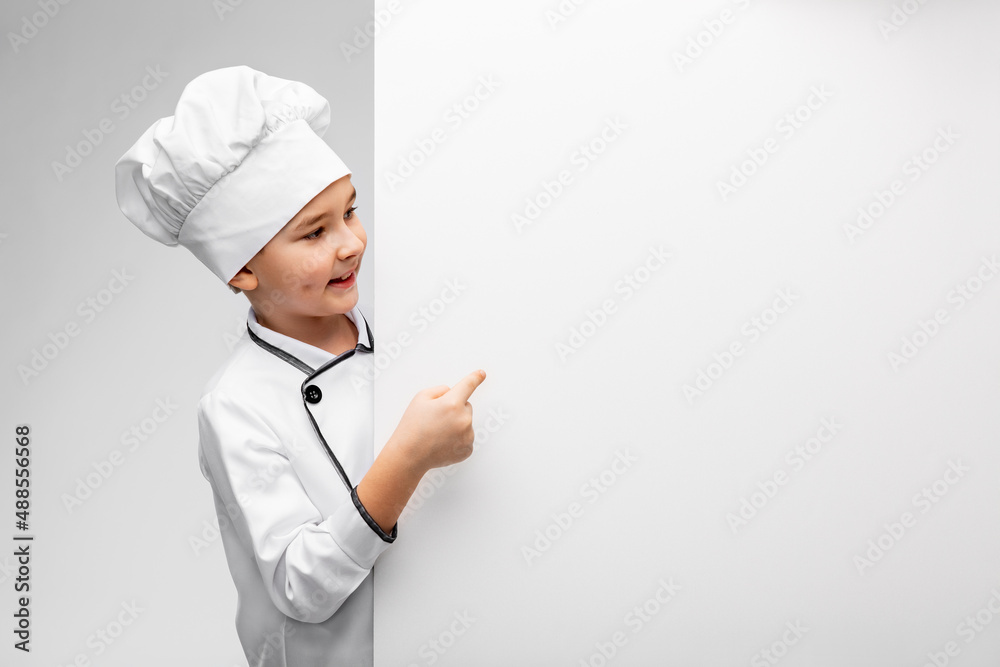 cooking, culinary and profession concept - happy smiling little boy in chef's toque and jacket showing white board over grey background cooking, culinary and profession concept - happy smiling little boy in chef's toque and jacket showing white board over grey background