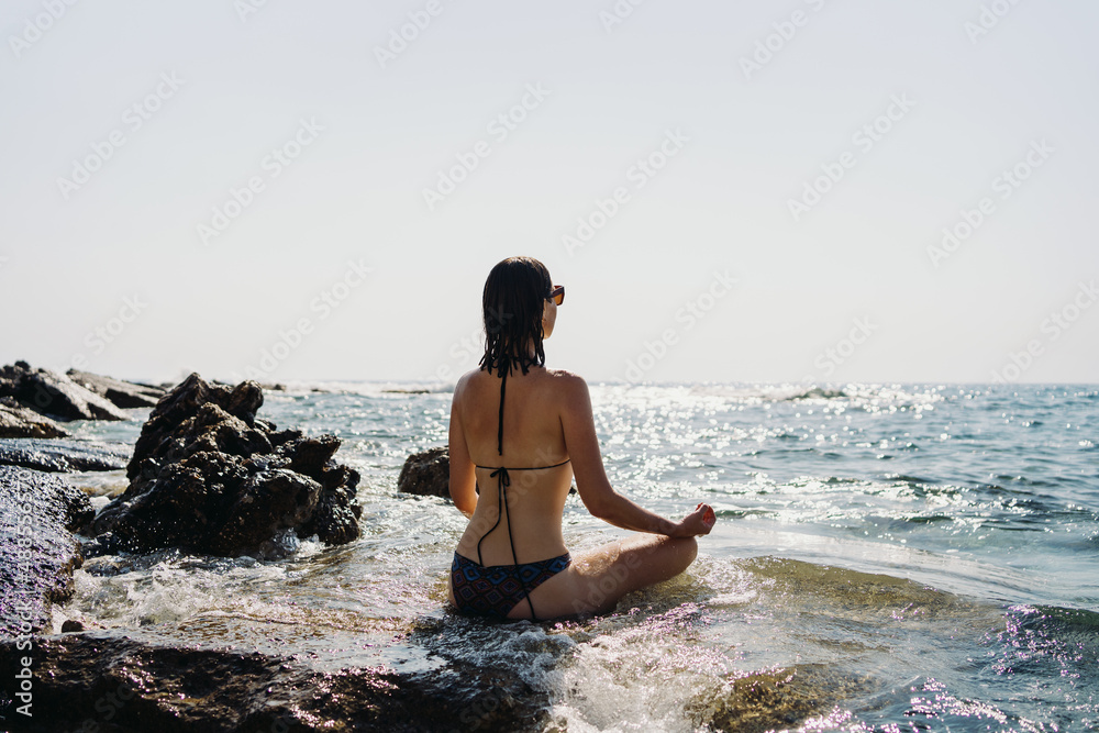 Happy young woman enjoying freedom on vacation while sitting on the coast rocks enjoying sea and blue sky view Happy young woman enjoying freedom on vacation while sitting on the coast rocks enjoying sea and blue sky view