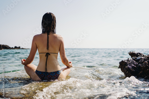 Happy young woman enjoying freedom on vacation while sitting on the coast rocks enjoying sea and blue sky view