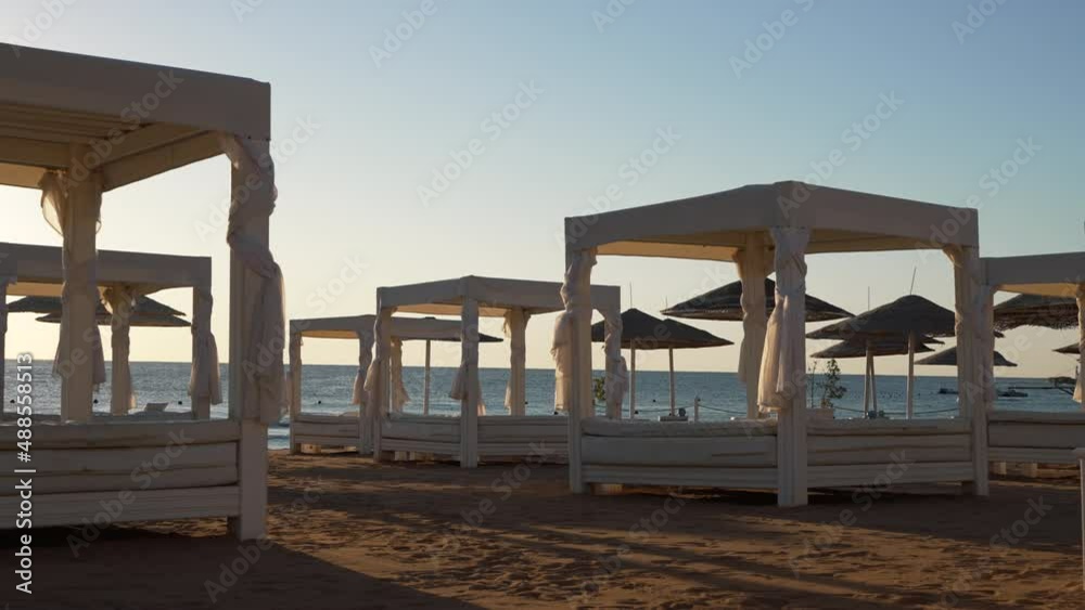 Beach tents with tied curtains on sandy seashore at sunset, waves in the distance, clear sky above. Relaxing in beautiful nature, summer holidays, luxury recreation Beach tents with tied curtains on sandy seashore at sunset, waves in the distance, clear sky above. Relaxing in beautiful nature, summer holidays, luxury recreation