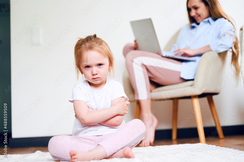 Upset little girl sitting lonesome while mother using laptop. Mother don't have time for daughter Upset little girl sitting lonesome while mother using laptop. Mother don't have time for daughter