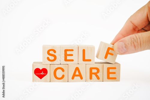 self-care word and red heart with heartbeat on wooden blocks with hand holding f alphabet cube for take care of yourself, good health concept