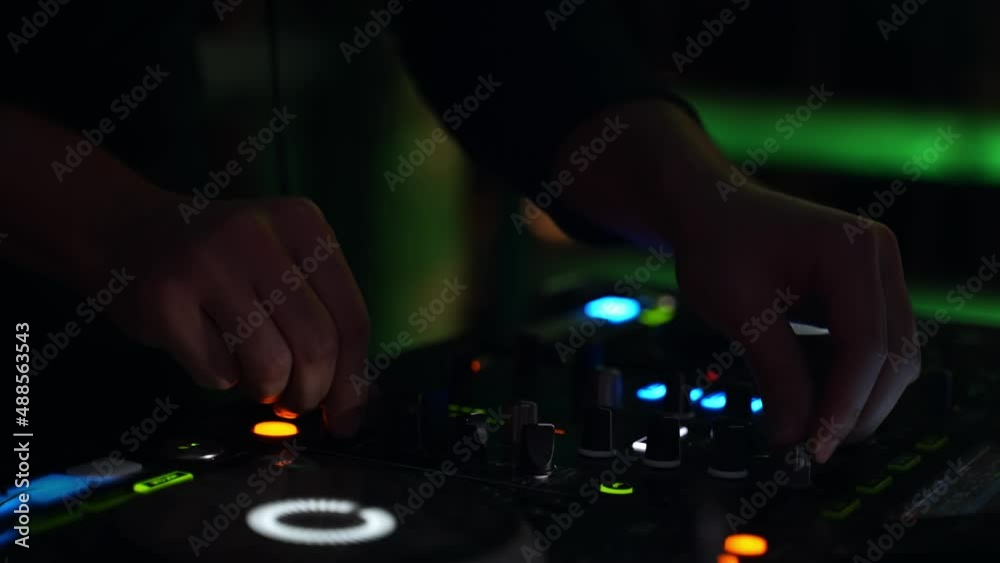 Close up of hands of a DJ turning buttons of his digital mix table at night. Spinning music track lights and colorfull background Close up of hands of a DJ turning buttons of his digital mix table at night. Spinning music track lights and colorfull background
