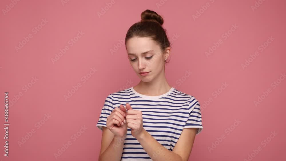Beautiful woman with bun hairstyle looking at her nails, admiring with fresh manicure, enjoying beauty procedures, self care, wearing striped T-shirt. Indoor studio shot isolated on pink background. Beautiful woman with bun hairstyle looking at her nails, admiring with fresh manicure, enjoying beauty procedures, self care, wearing striped T-shirt. Indoor studio shot isolated on pink background.