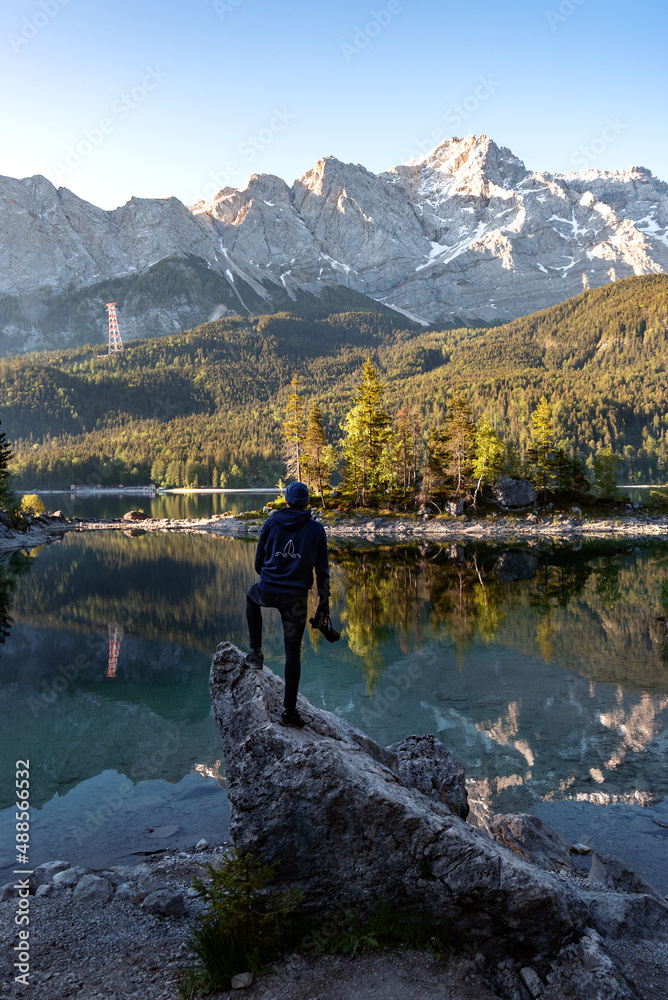 Hiker at Eibsee lake with Zugspitze mountain at sunrise. Sunny outdoor scene in German Alps, Bavaria, Germany, Europe. 
