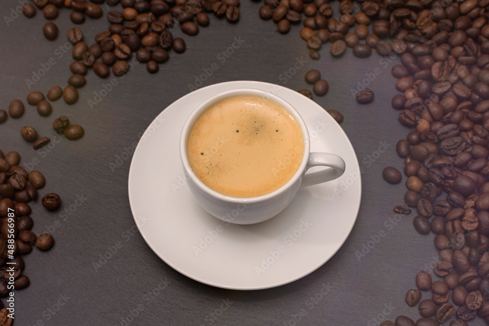 Obraz premium white cup with espresso coffee on a saucer with coffee beans on a dark background