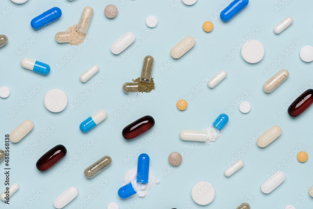 Pills pattern with some capsules open and drug content spilled top view on blue background Pills pattern with some capsules open and drug content spilled top view on blue background