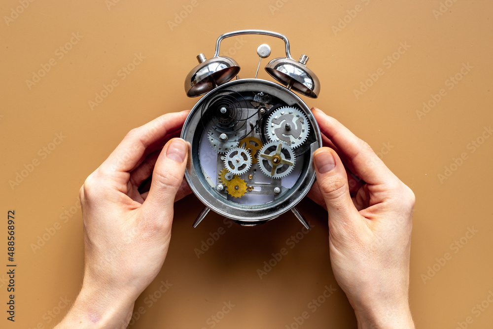 Hands holding alarm clock mechanism with steel gears and wheels close up