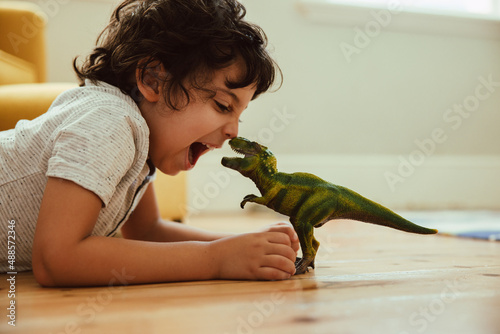 Adventurous young boy imitating a t-rex dinosaur toy at home photo