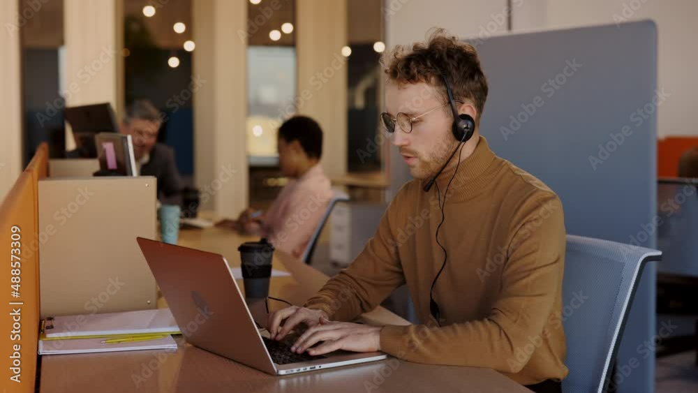 Smiling caucasian man wearing wireless headset making conference video call on laptop. Male professional call center agent, hr manager having distance webcam chat job interview on computer at office. Smiling caucasian man wearing wireless headset making conference video call on laptop. Male professional call center agent, hr manager having distance webcam chat job interview on computer at office.
