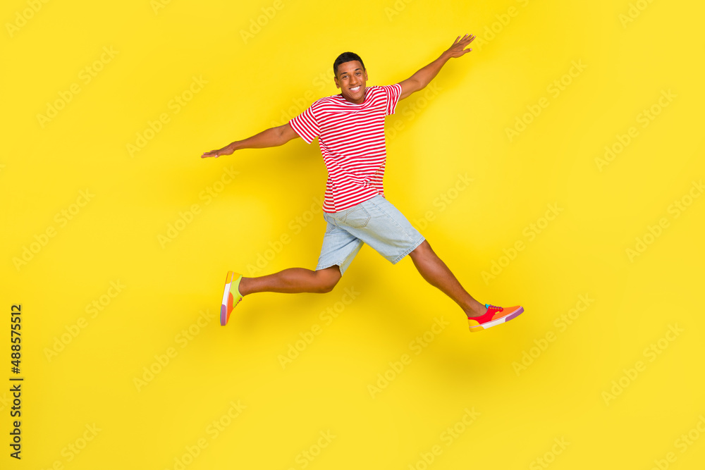 Full length profile side photo of guy jump raise hands aside run wear red striped footwear isolated over yellow color background