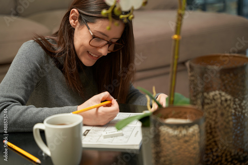 Photos Woman playing sudoku game at home in a game book, alone