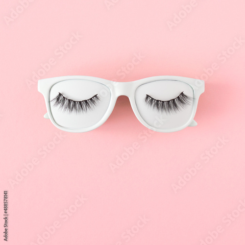 White tinted sunglasses and lashes on pastel pink background, flat lay. Minimal summer concept.