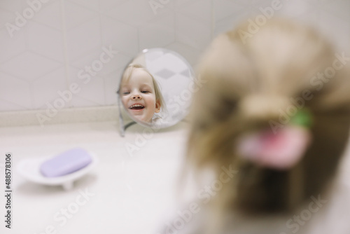 little funny girl brushing teeth and washing hands in the bathroom, reflection in the mirror.