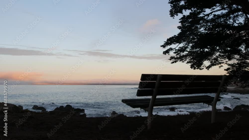 Ocean beach, empty bench silhouette on shore, sea water waves, Monterey, 17-mile drive, California coast, USA. Pacific Grove beachfront waterfront promenade, waterside park, sunset seascape, pine tree Ocean beach, empty bench silhouette on shore, sea water waves, Monterey, 17-mile drive, California coast, USA. Pacific Grove beachfront waterfront promenade, waterside park, sunset seascape, pine tree