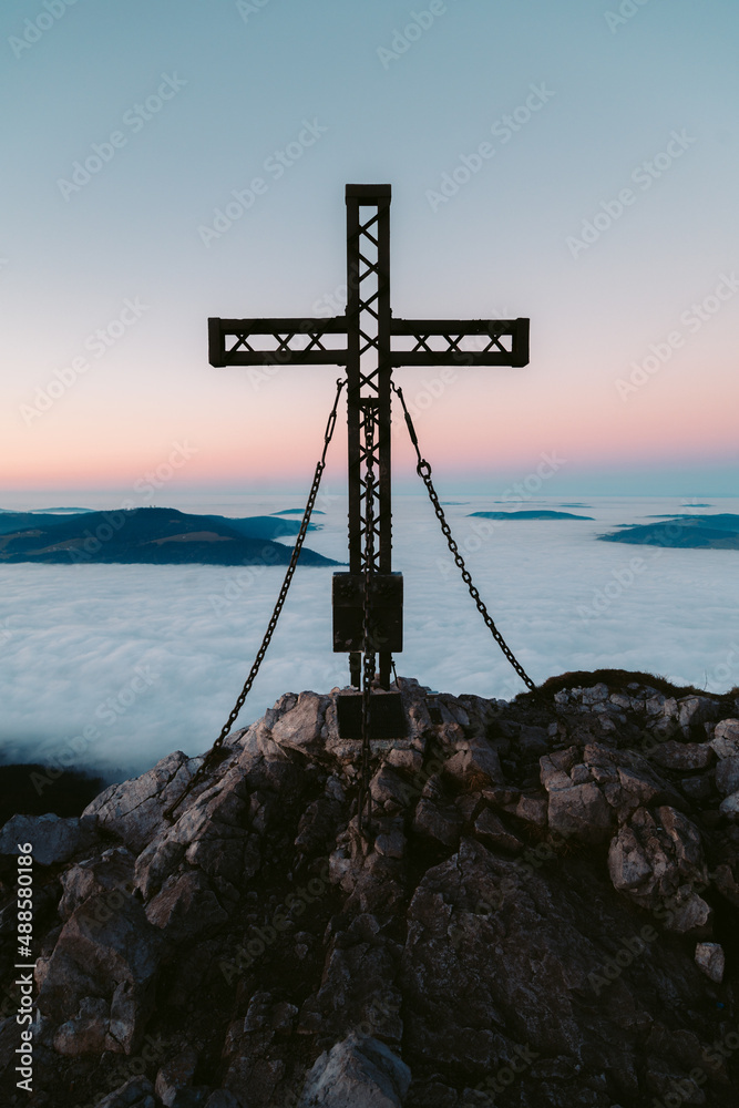Summit cross on mountain peak above sea of clouds at dusk