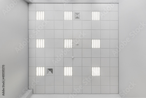 cassette suspended ceiling with square halogen spots lamps and drywall construction in empty room in apartment or house. Stretch ceiling white and complex shape. Looking up view