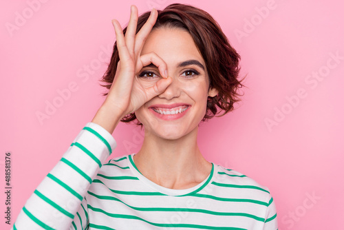 Portrait of attractive cheerful girl showing ok-sign like watch look see isolated over pink pastel color background