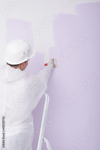a man in a white helmet paints a white wall lilac