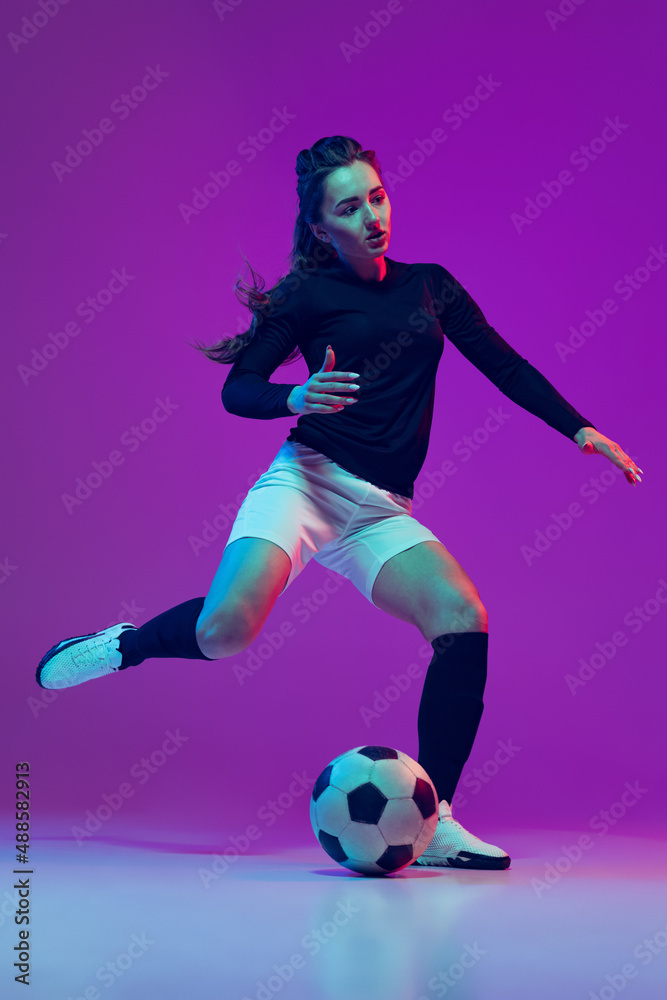 Professional female soccer player dribbling football ball isolated on purple studio background in neon light. Sport, action, motion, fitness