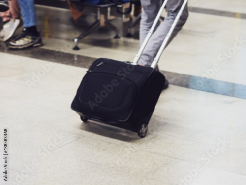 A black bag on wheels is carried by a traveler across the marble floor. Airplane passengers at the airport. Defocused image