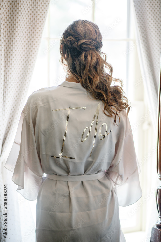 Bride in a white wedding robe with words " I Do" on the back Morning of