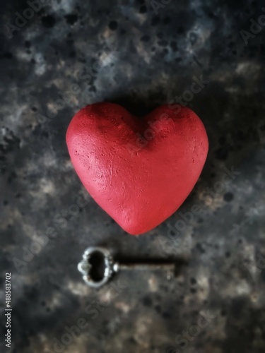 red heart and vintage key on rusty concrete background with copy space and selective focus