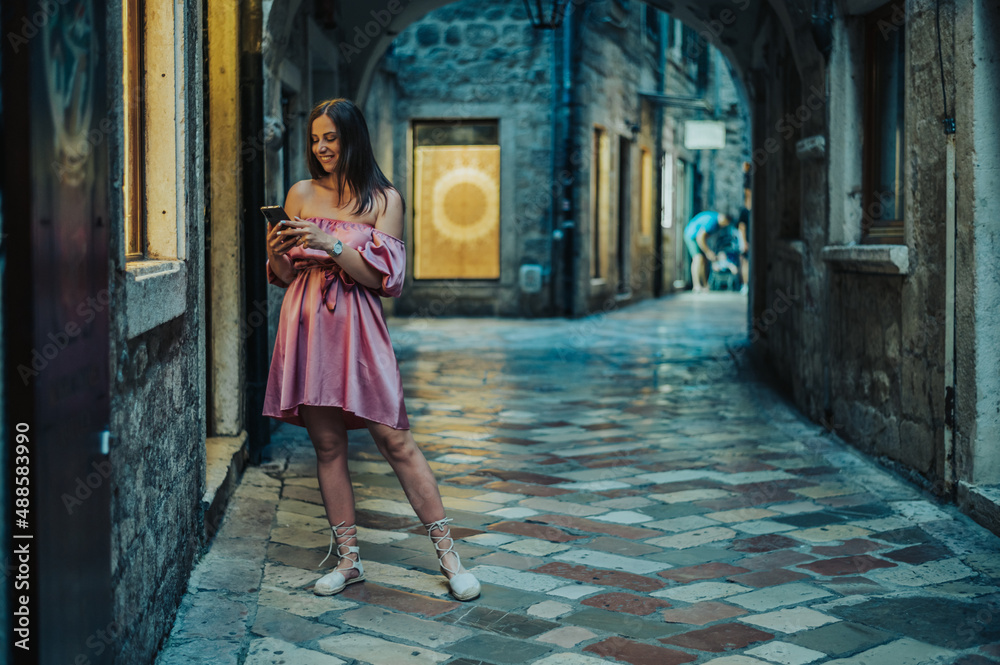 Beautiful young woman using smartphone while walking on the city streets on the coast during the night