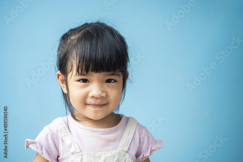 A headshot portrait of a cheerful baby Asian woman, a cute toddler little girl with adorable bangs hair, a child wearing a purple sweater smiling and looking to the camera.
