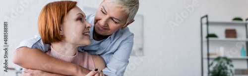 smiling lesbian women looking at each other at home, banner