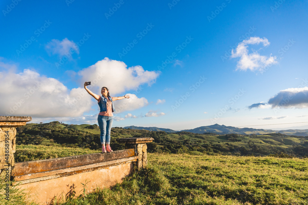 Beautiful caucasian latina woman taking a selfie on a wall with a landscape in the background 