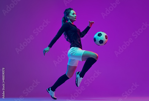 Dynamic portrait of female soccer player practicing with football ball isolated on purple studio background in neon light. Sport, action, motion, fitness © master1305