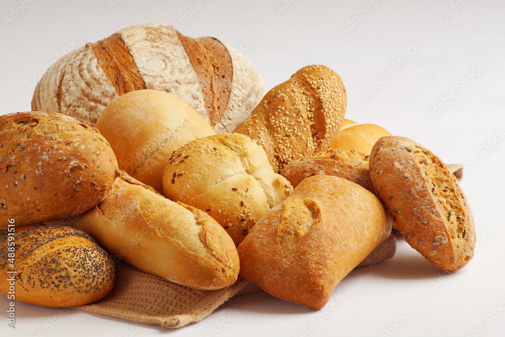 various types of freshly baked with a crispy crust bakery products - rye bread, wheat, bread, baguette, ciabatta, buns - lie on a table covered with a kitchen towel