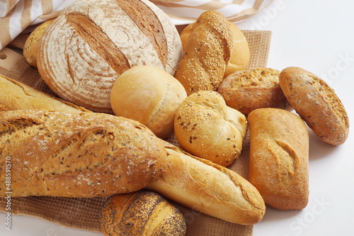 In a towel, on a wooden cutting board are different types of freshly made bread - round bread, baguette, ciabatta, buns