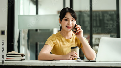 Attentive asian woman sit at desk and call the phone at coffee cafe.
