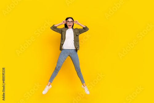 Full length photo of impressed young lady jump wear eyewear shirt jeans shoes isolated on yellow background