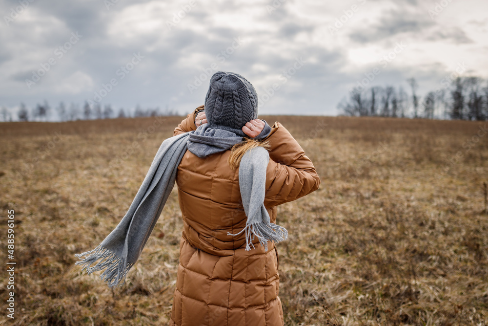 Wind and cold weather. Woman wearing coat, scarf and knit hat outdoors