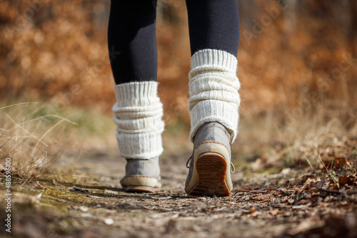Kintted leg warmers on hiking boot. Woman walking on footpath in forest
