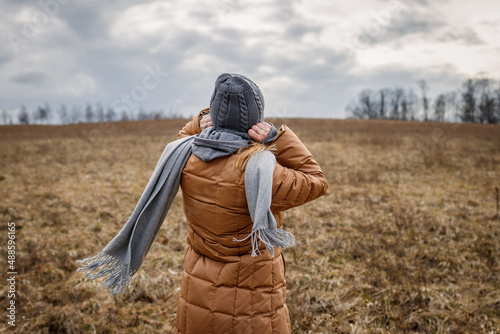 Wind and cold weather. Woman wearing coat, scarf and knit hat outdoors