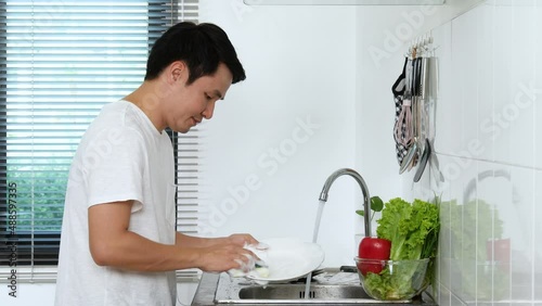 Happy young man washing dishes in the sink in the kitchen at home